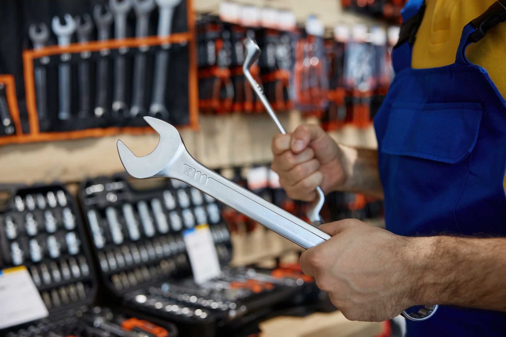 Person holding a wrench in a tool shop, with shelves of tools in the background