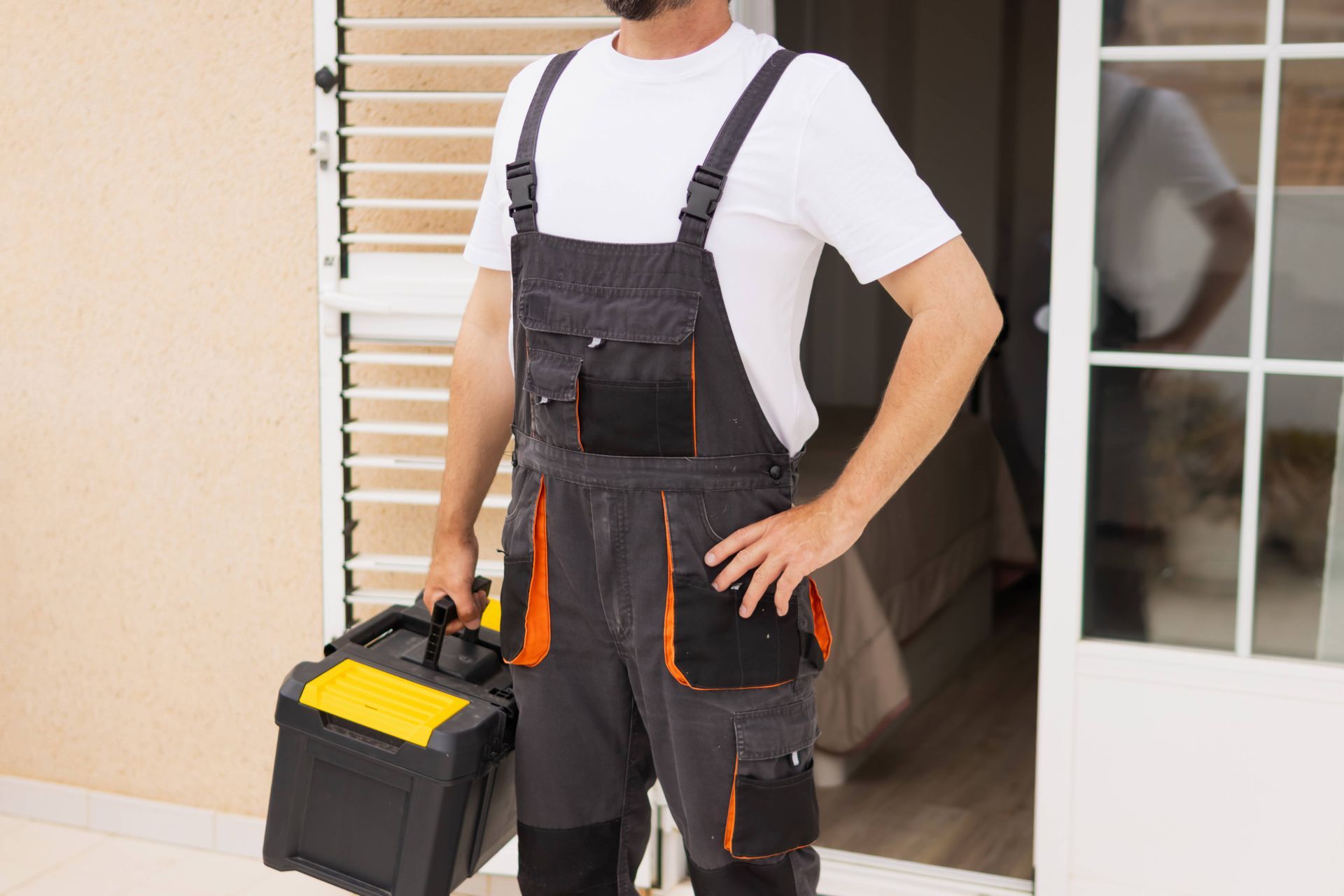 Person in dark overalls carrying a toolbox outside a doorway