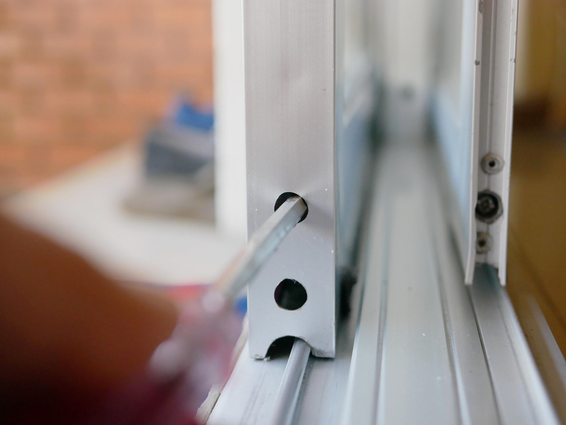 Close-up of a window latch and white frame with a screwdriver adjusting a screw