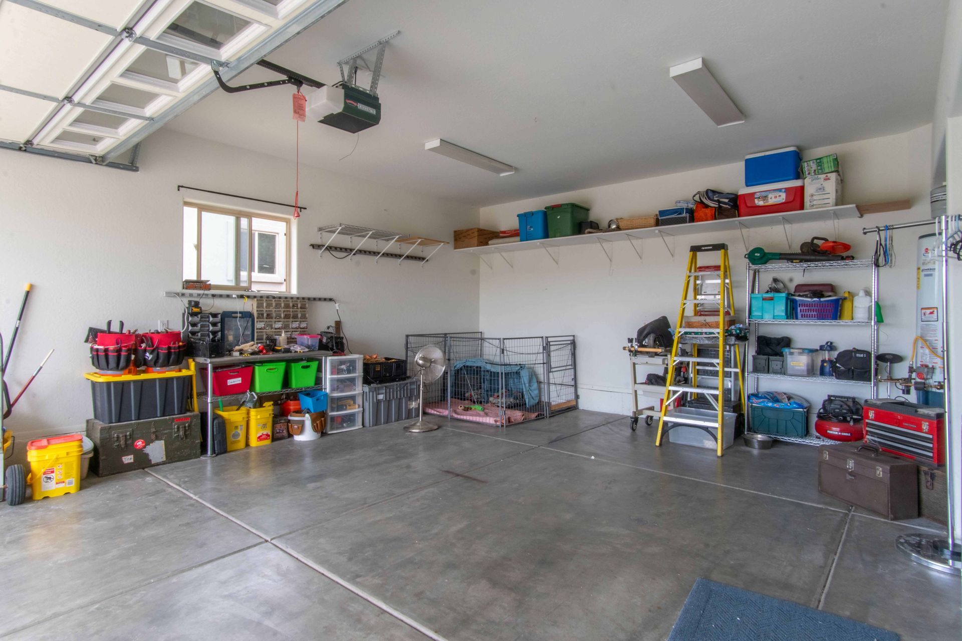 Organized garage with concrete floor, shelves, tools, storage bins, and a ladder along the wall
