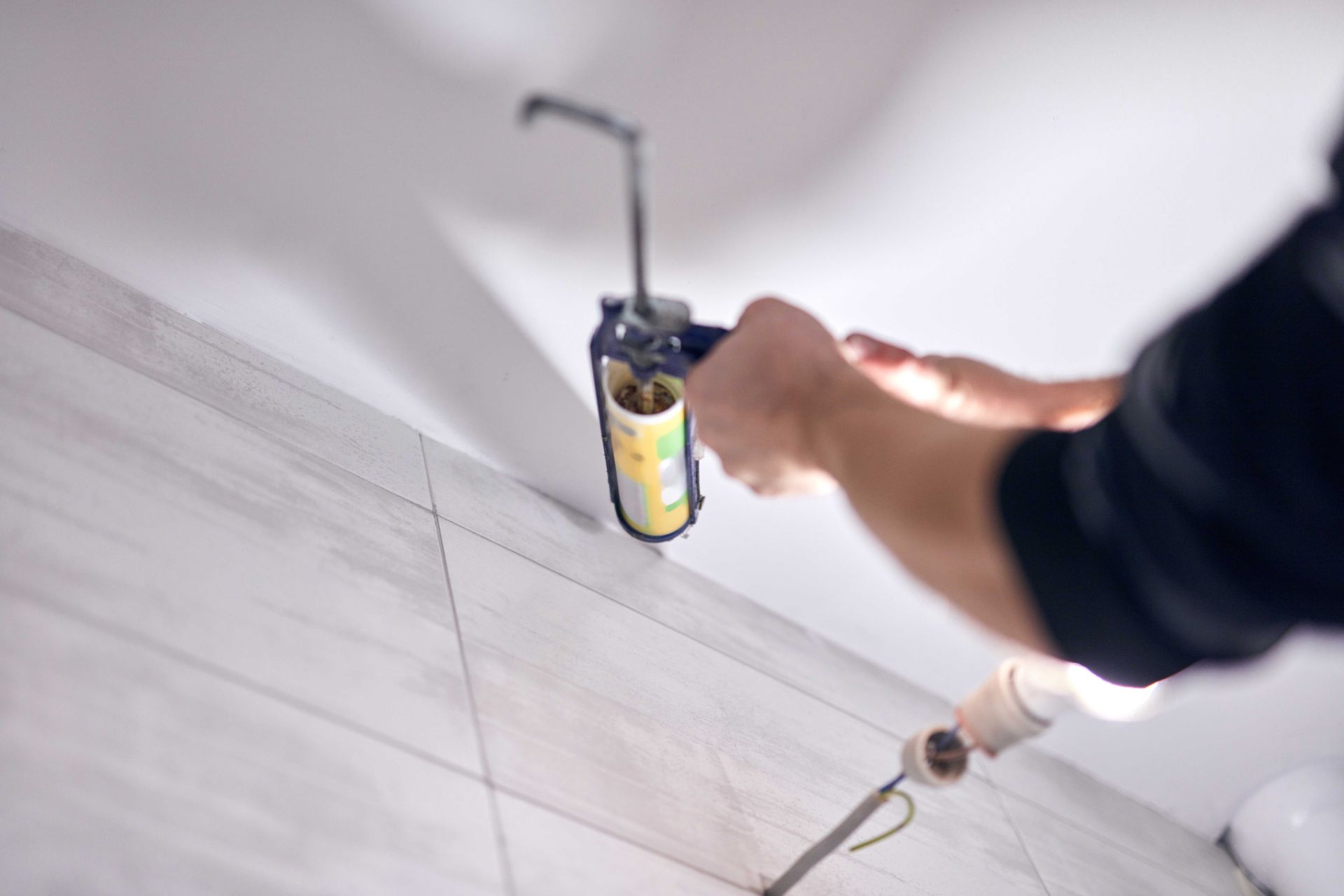 Person applies sealant to white tiled floor with a caulking gun and spray bottle nearby