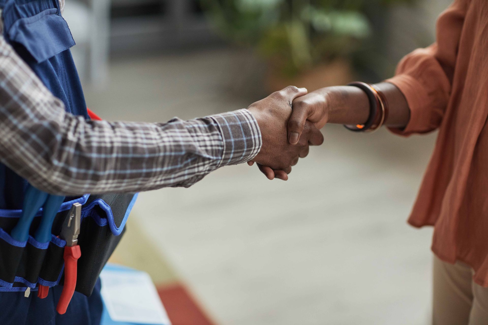 Two people shaking hands outdoors, one in a blue plaid shirt and the other in an orange sleeve