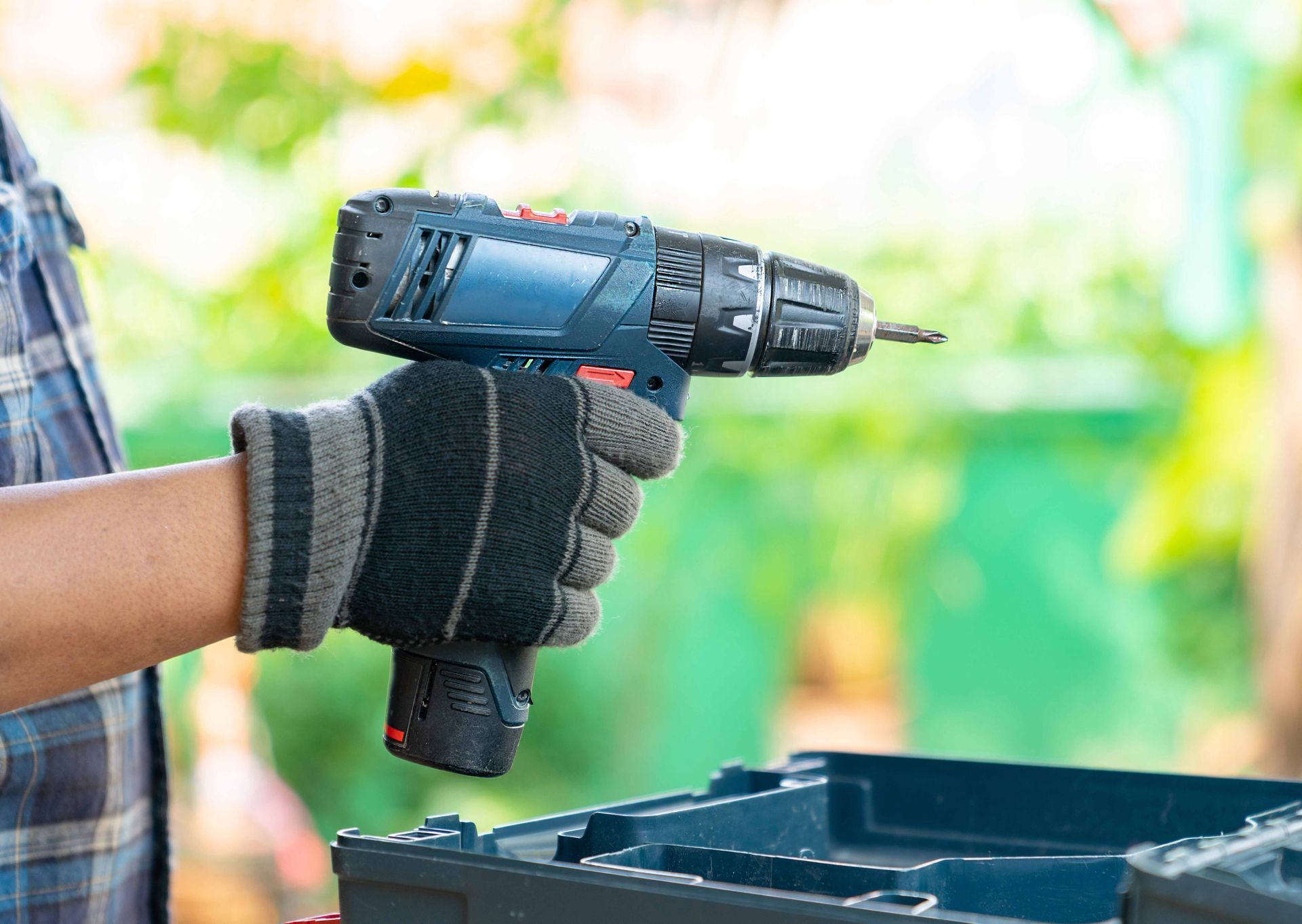 Gloved hand holding a cordless drill over a toolbox outdoors