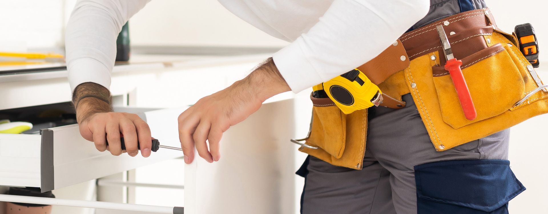 Two plumbers working under a sink with tools in a kitchen cabinet