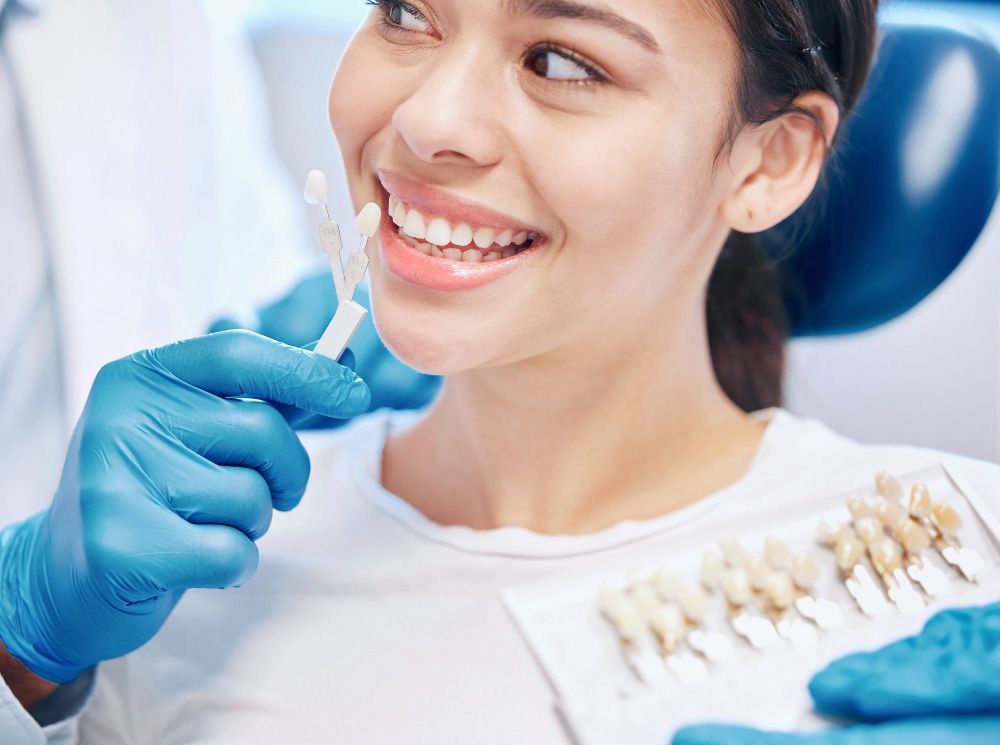 Dentist wearing blue gloves examines a smiling patient in a dental chair