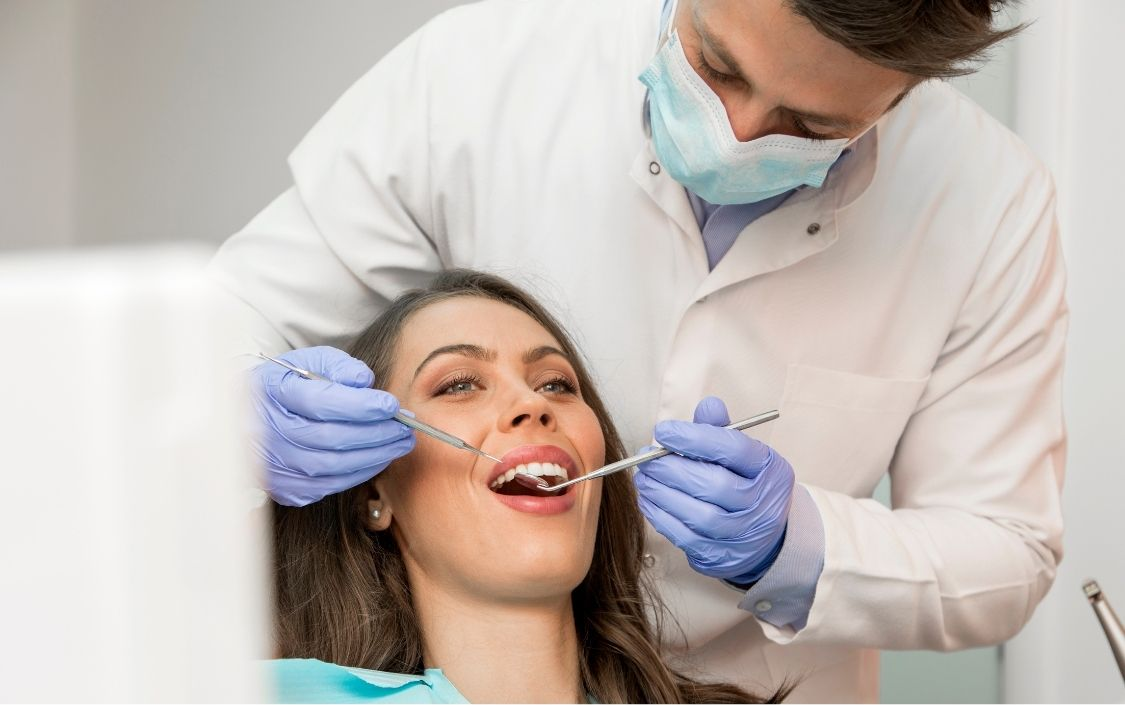 Dentist examining a patient’s teeth with a mirror and gloved hands in a clinic