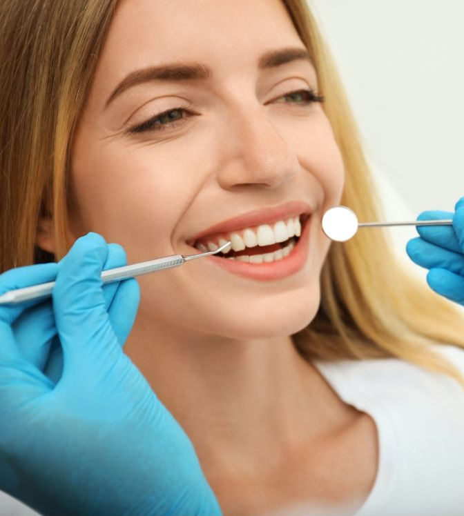 Dental professional examining a smiling patient’s teeth with a mirror and tool, wearing blue gloves