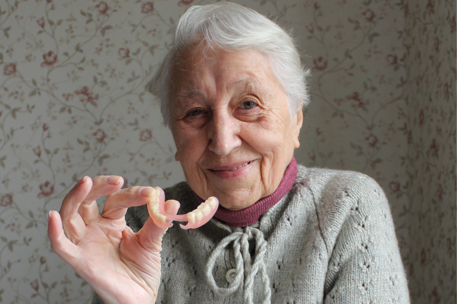 Close-up of a person holding a pink denture near their open mouth
