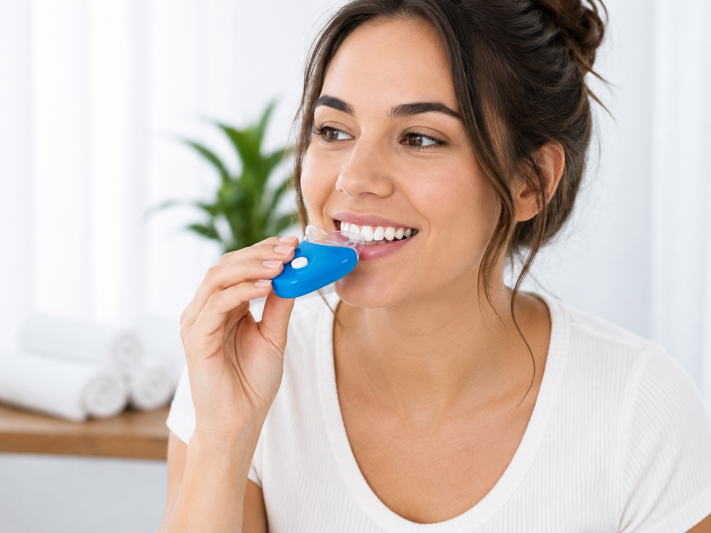 Woman smiling while using a blue teeth-whitening device in a bright room