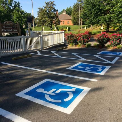 Worker using line striping machine to apply white line on asphalt parking lot for traffic control
