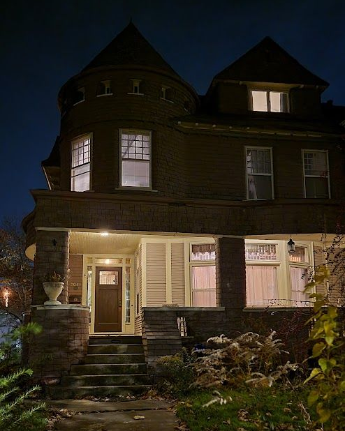 Brown house at night, lit windows. Stone steps lead to a porch and front door. Dark blue sky.