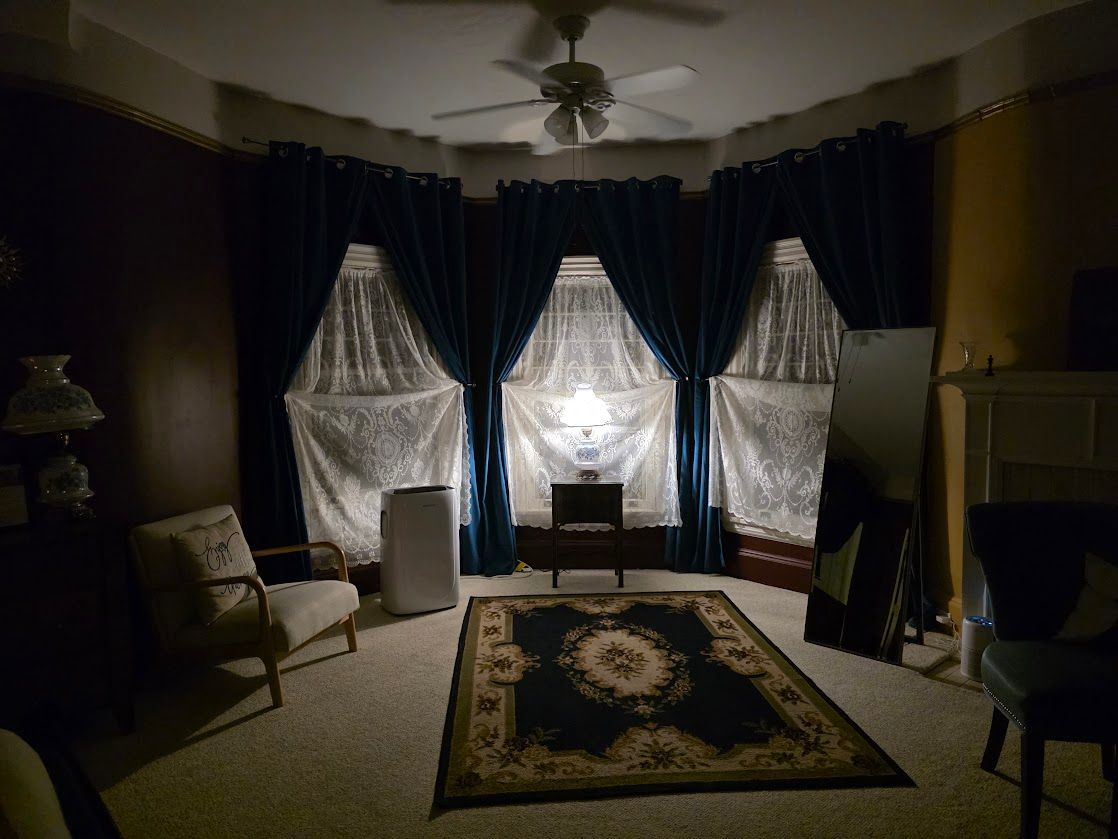 A dimly lit room with blue curtains and a patterned rug.