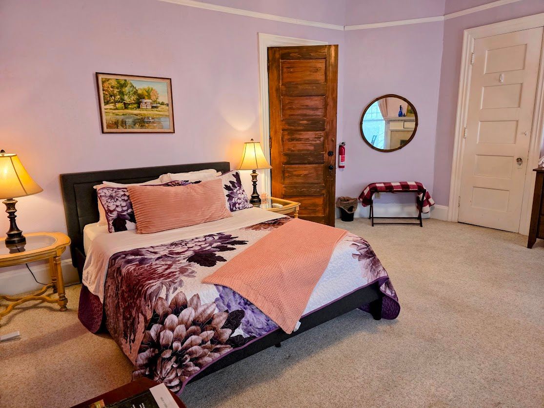 Bedroom with purple walls, bed with floral comforter, nightstands, and a wooden door.