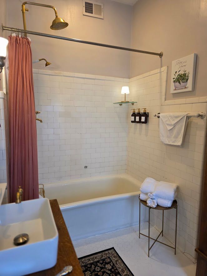 A bright bathroom with a white subway-tile bathtub, gold shower fixtures, a pink curtain, and a rectangular sink.