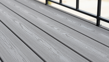 Gray wooden deck boards beside a black metal railing on a balcony