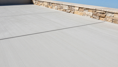 Light gray concrete patio beside a stone retaining wall in bright sunlight