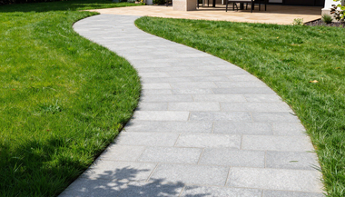 Curved light-gray stone walkway through green lawn toward a wooden deck