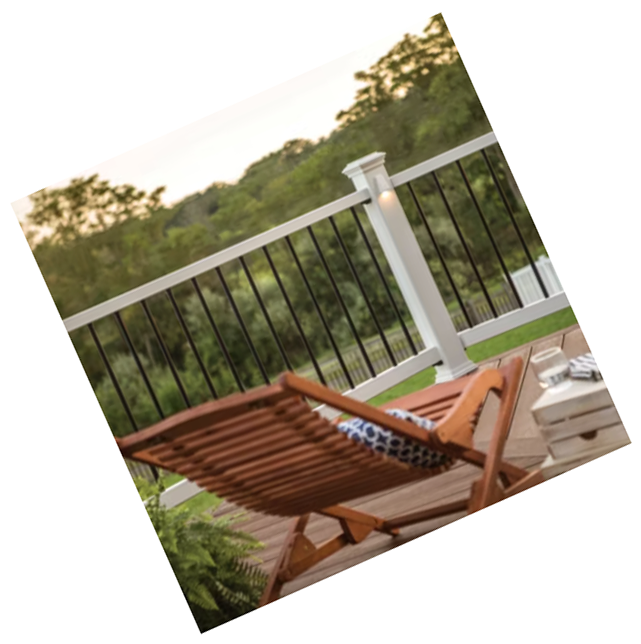 Wooden lounge chair on a sunlit deck with black railing and green trees in the background