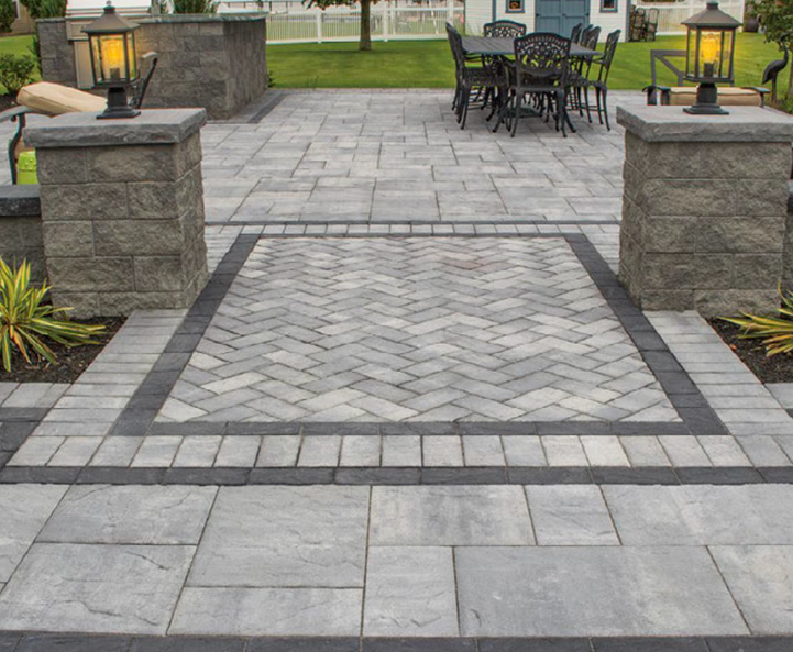Stone-paved patio with decorative lanterns and a black outdoor dining set in a landscaped yard