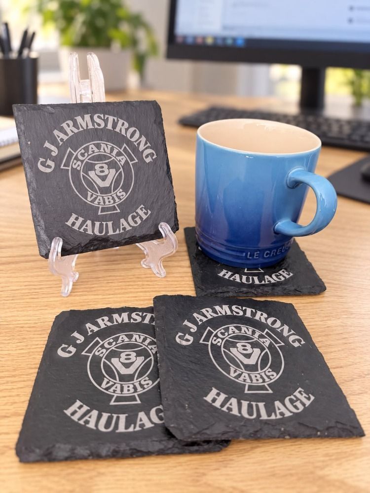 Personalised natural slate coasters engraved with G J Armstrong Haulage branding beside a blue mug