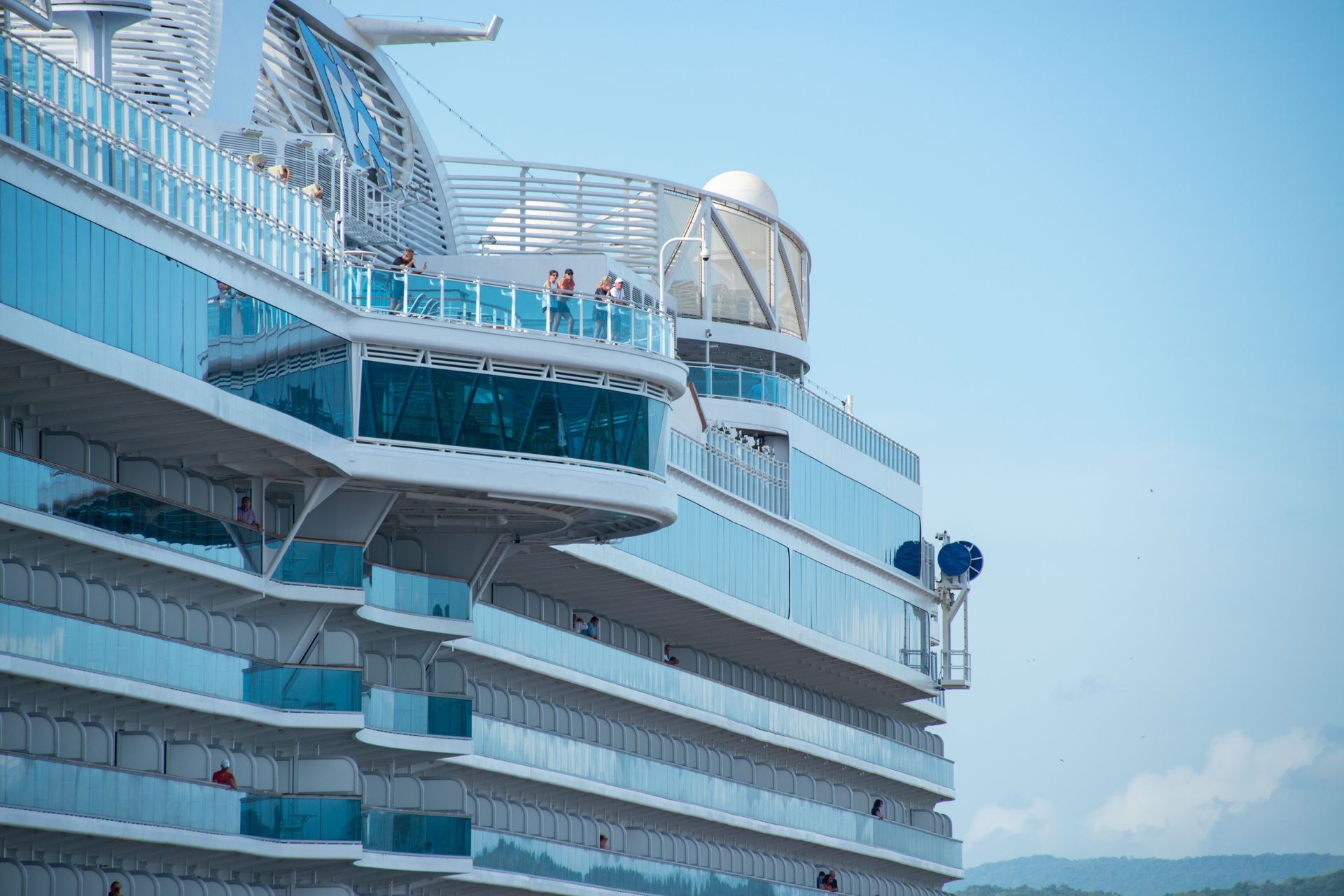 Large white cruise ship deck with blue windows and a ferris wheel on top against a clear sky