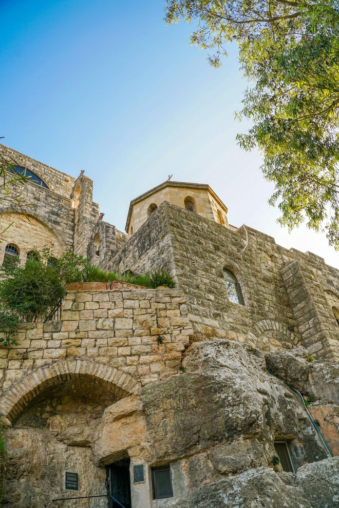 Stone monastery or fortress ruins on a rocky hillside beneath a clear blue sky and trees