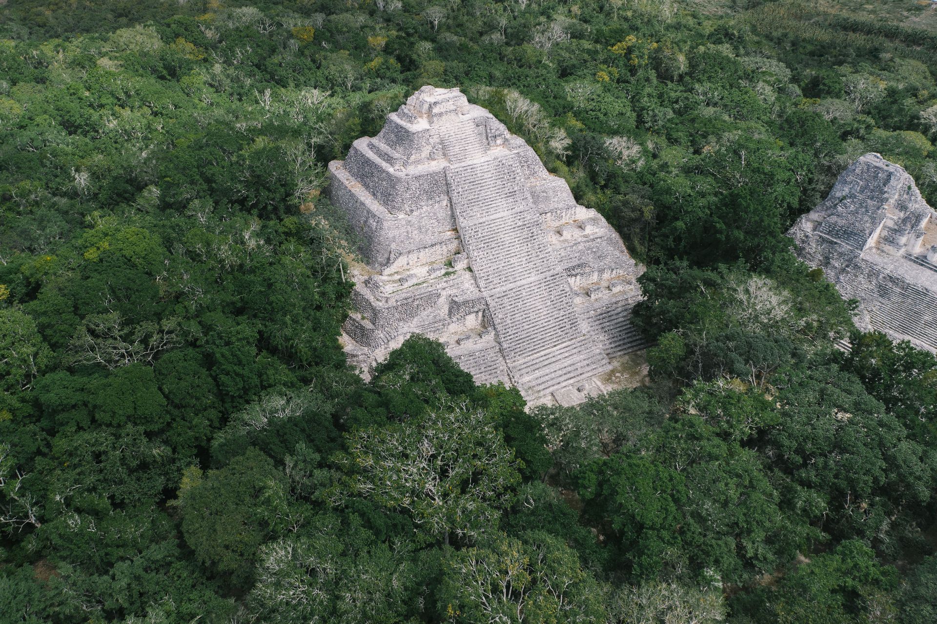 Aerial view of ancient stone pyramids emerging from dense green jungle vegetation