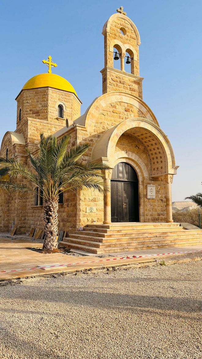 Small stone chapel with a yellow dome and arched entrance under a clear sky, beside a gravel path