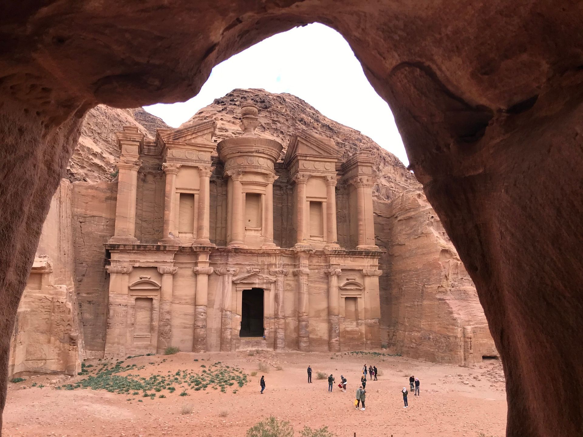 Cliffside buildings carved into a rocky desert canyon with a cave opening above