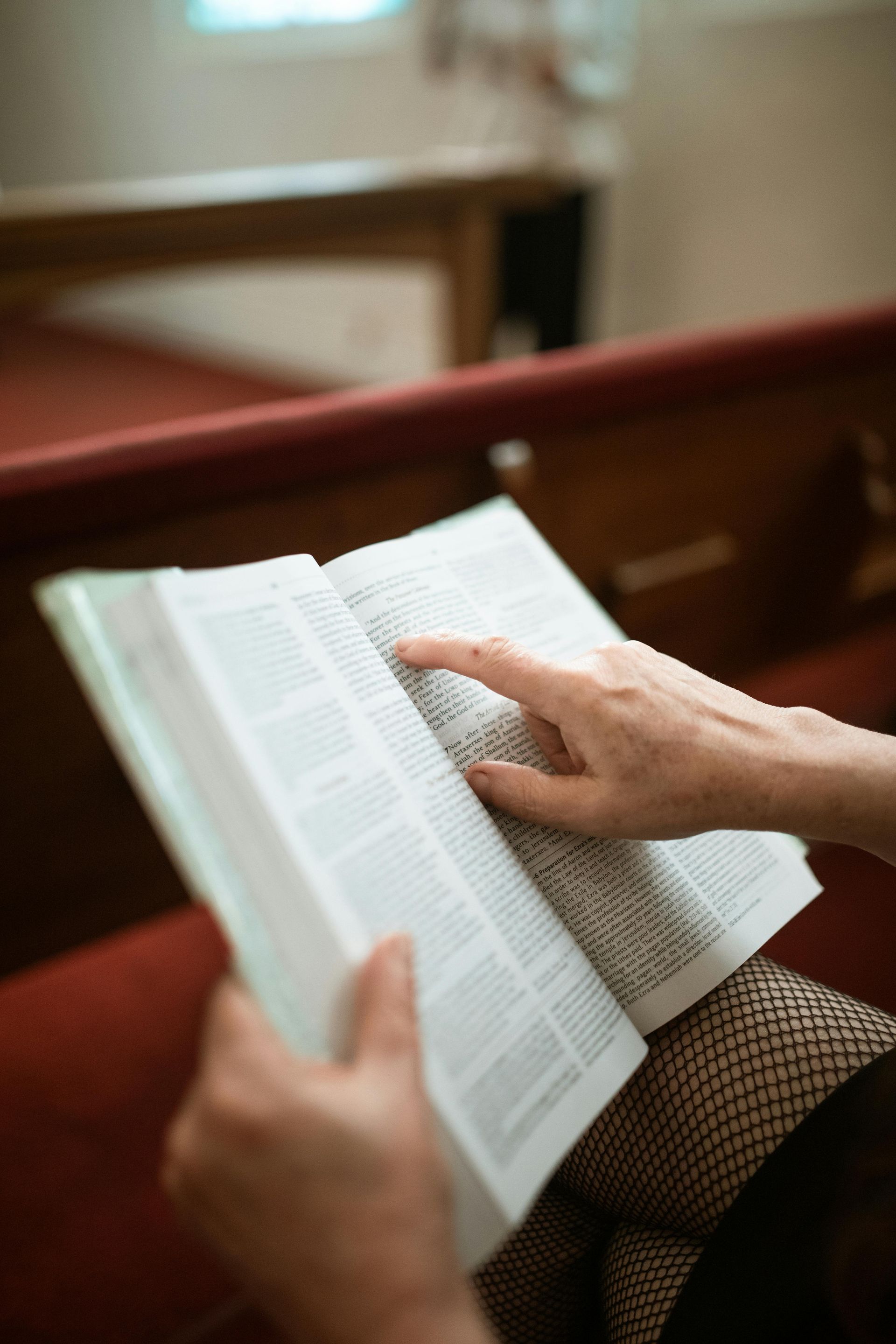 Hands turning pages of an open book in a red church pew