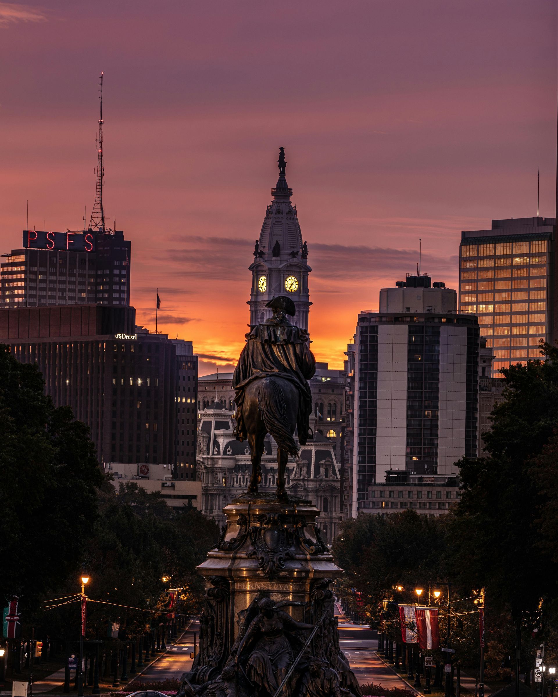 Sunset over a city skyline with a lit monument centered in the foreground