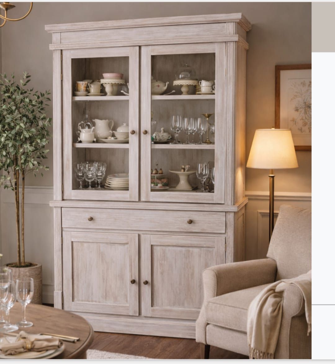 Vitrina blanca con vajilla en una acogedora sala de estar junto a una lámpara y un sillón beige.