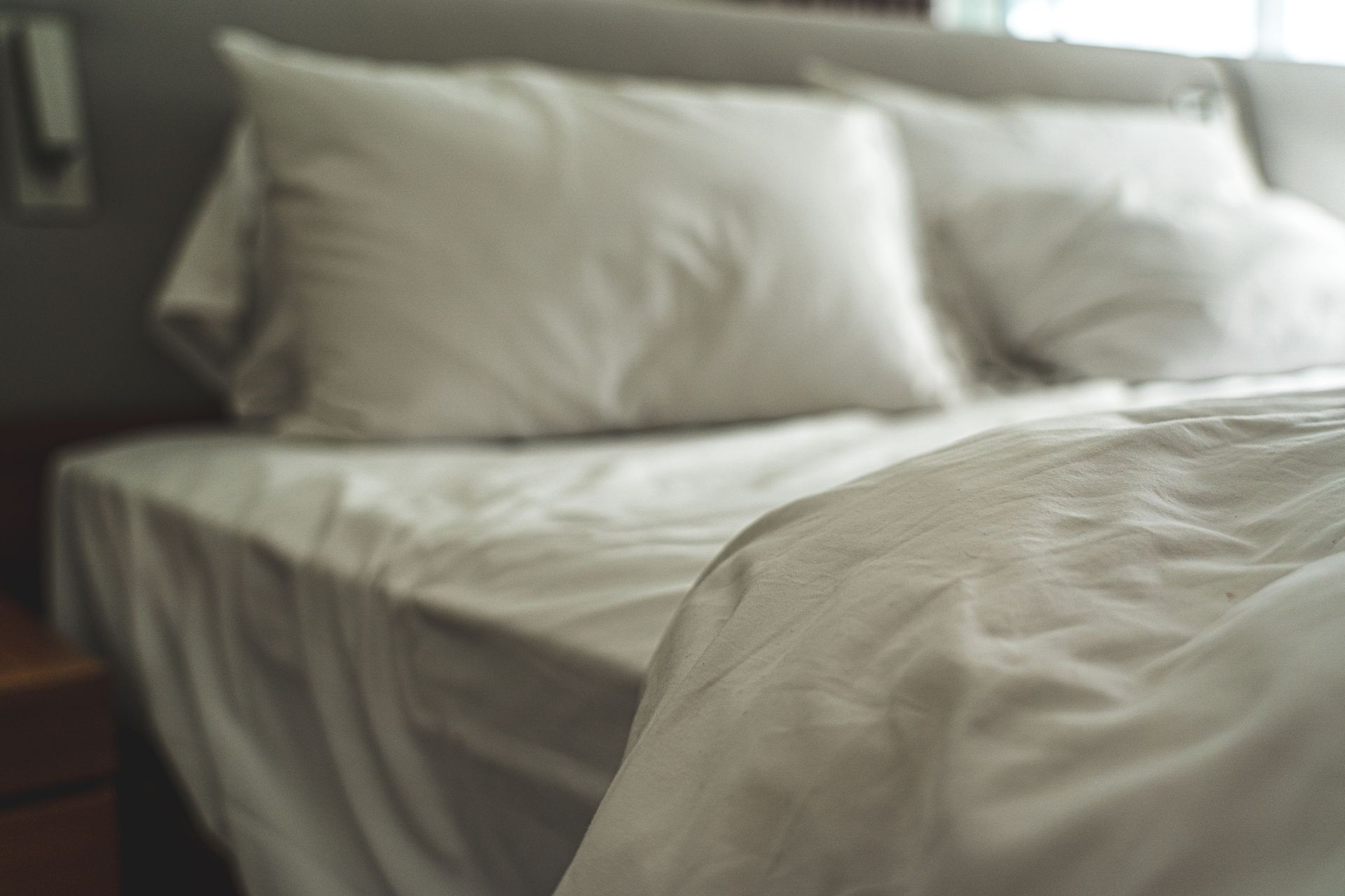 Cama deshecha con sábanas y almohadas blancas en un dormitorio con iluminación tenue.
