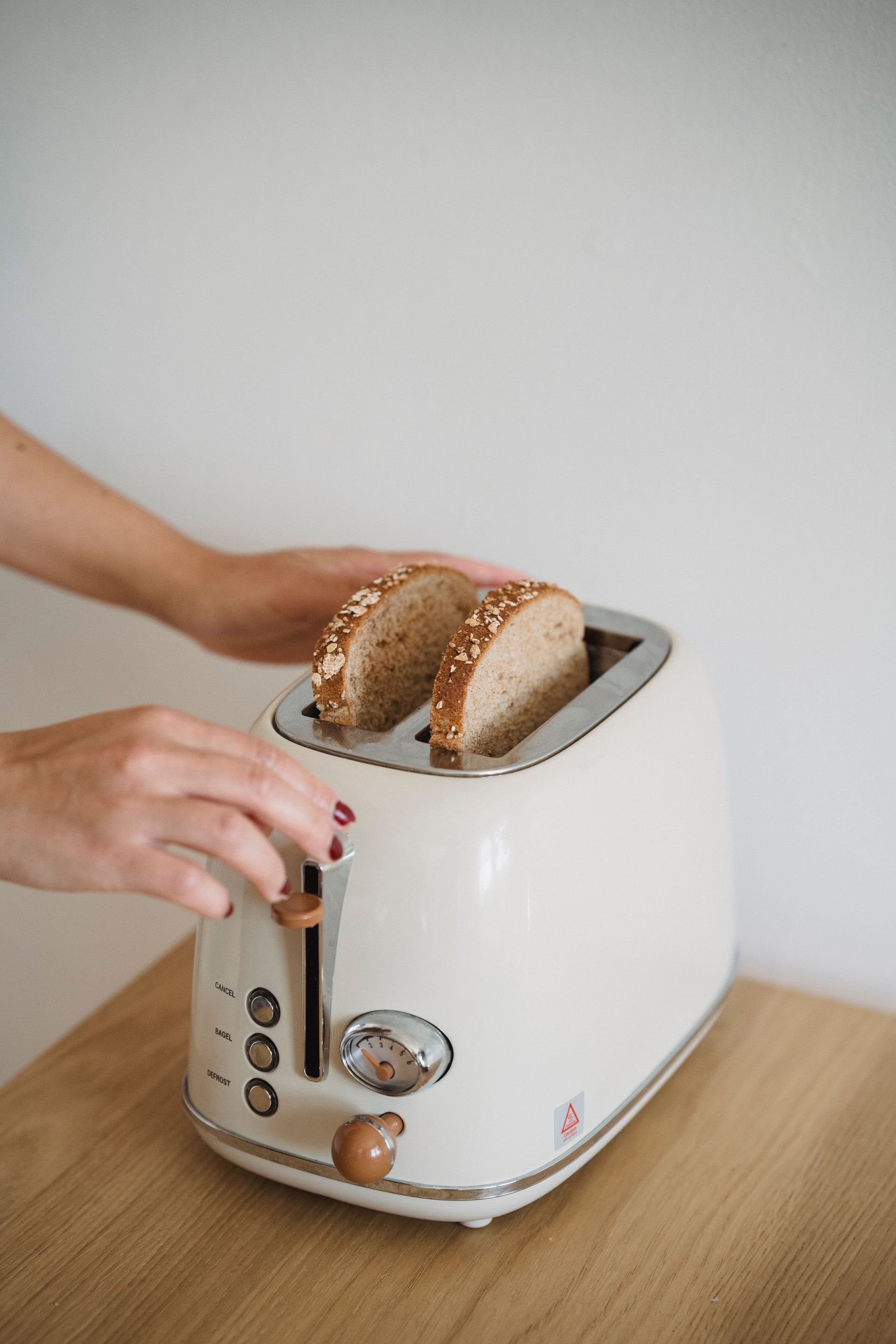 Unas manos colocan mitades de bagel en una tostadora blanca sobre una encimera de madera.