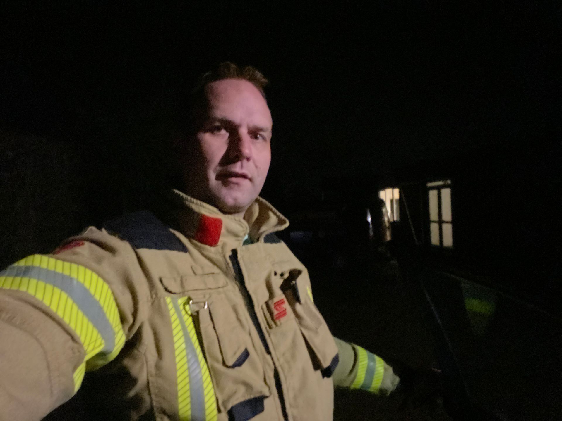 Brandweerman in uniform 's nachts, met het gebouw op de achtergrond.