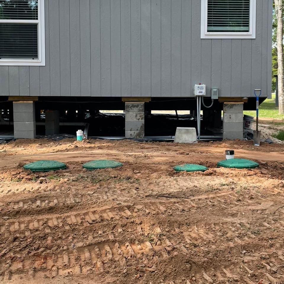 Elevated house on concrete piers over muddy ground with green utility covers and windows above the foundation