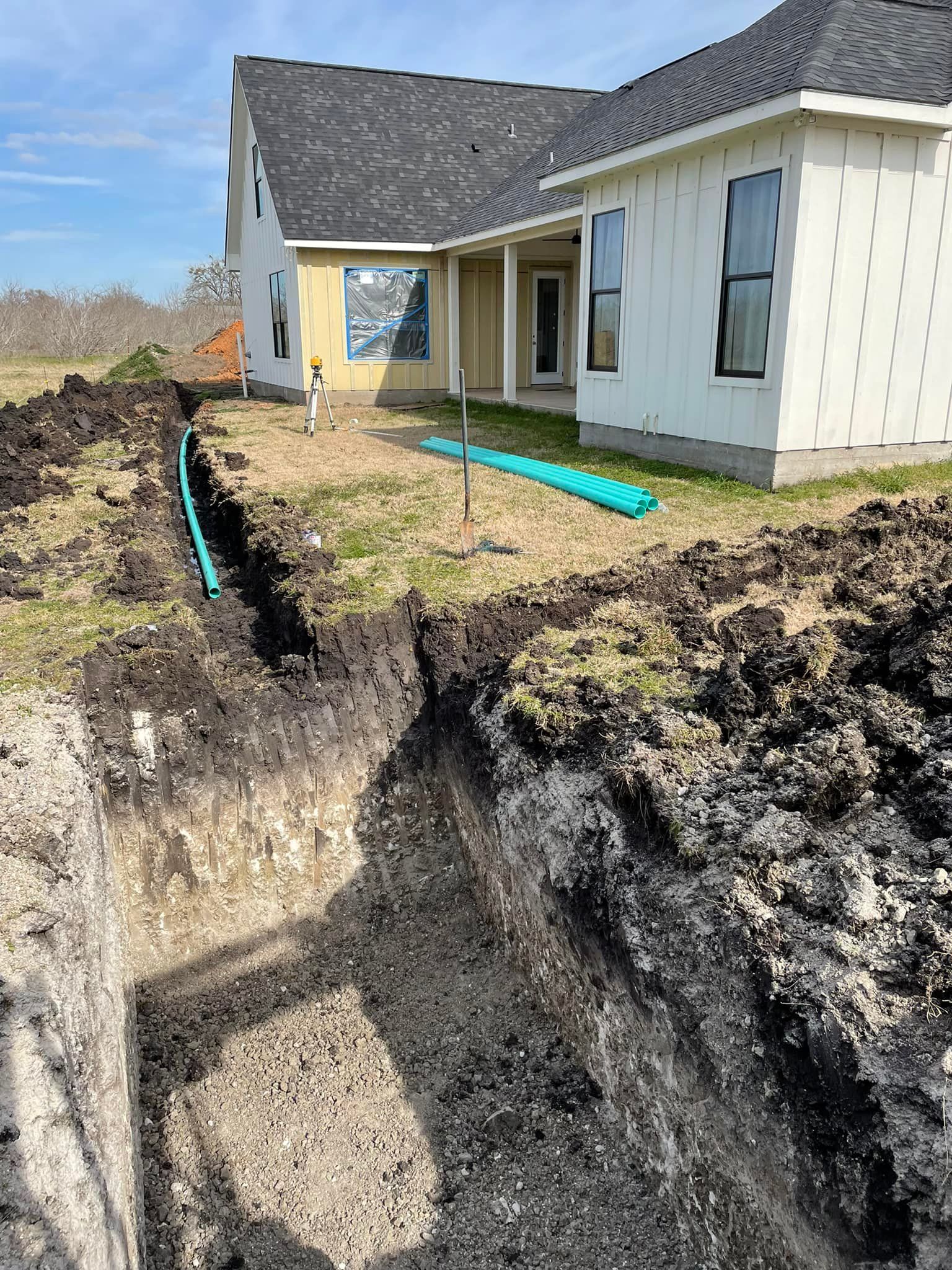 House foundation beside a deep excavation trench with exposed soil and blue drainage pipes