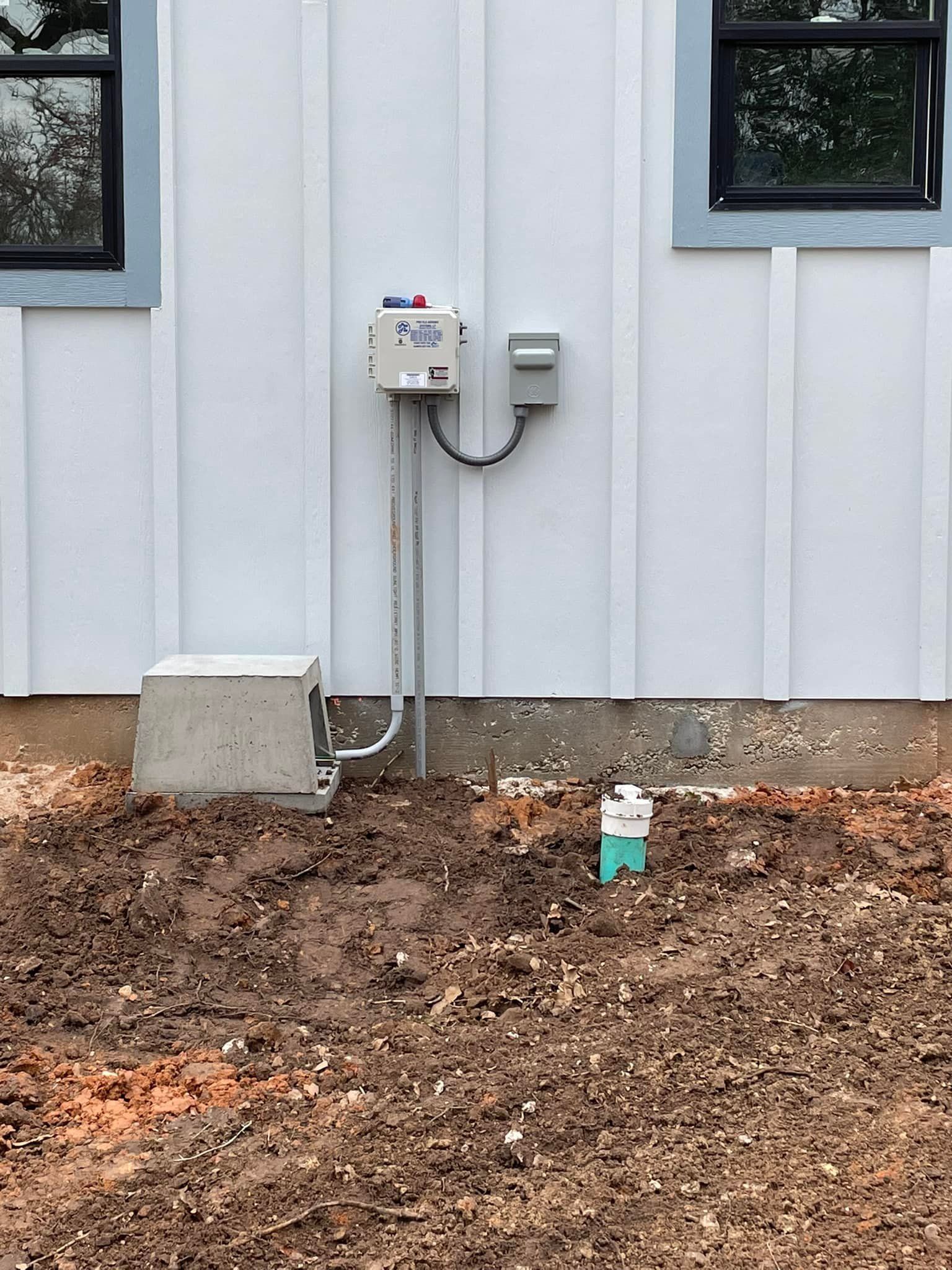 Exterior house wall with utility meter boxes, cables, and a dirt-covered ground beneath windows