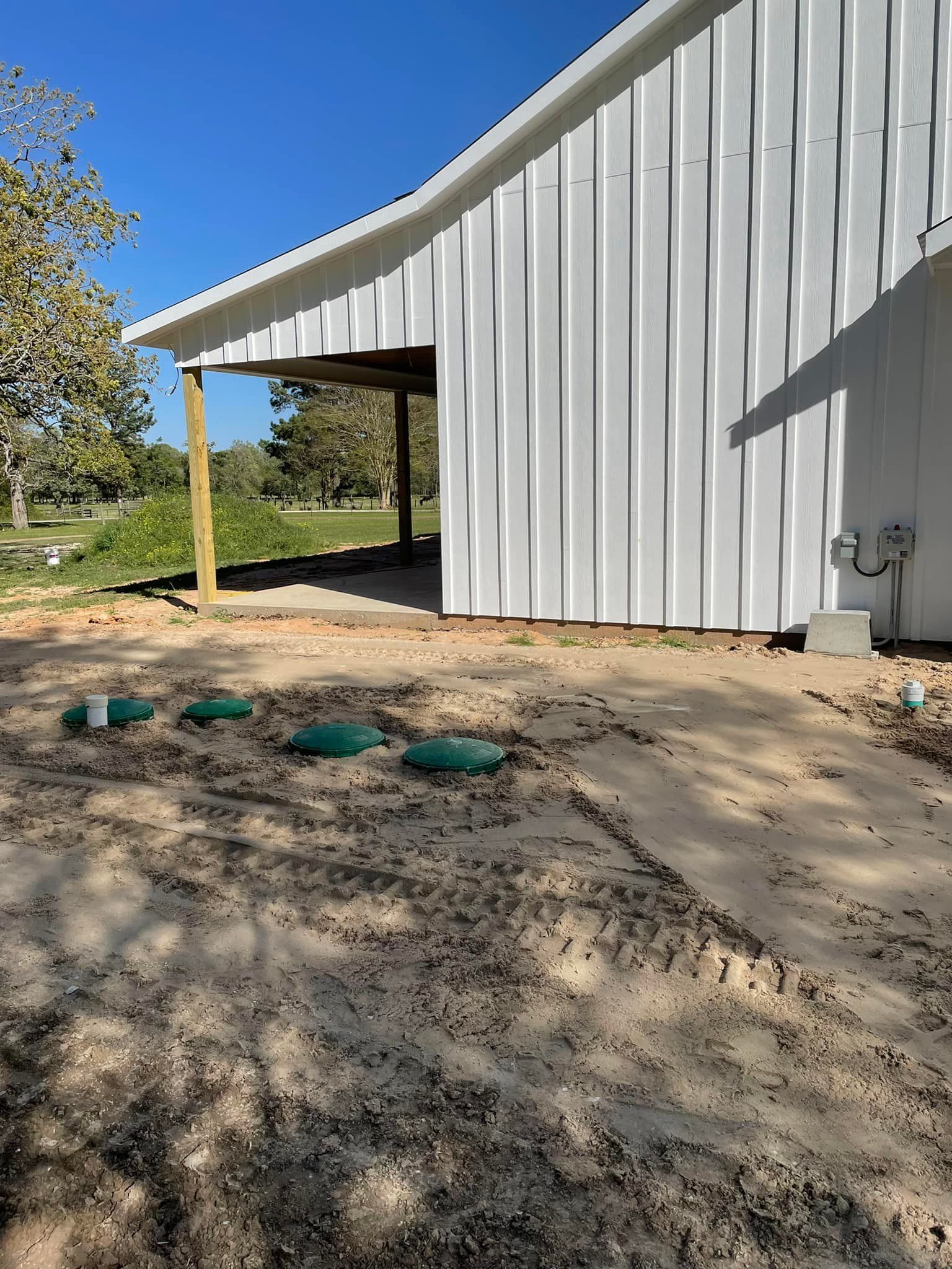 White metal building with a curved roof and green utility covers on bare ground under a blue sky