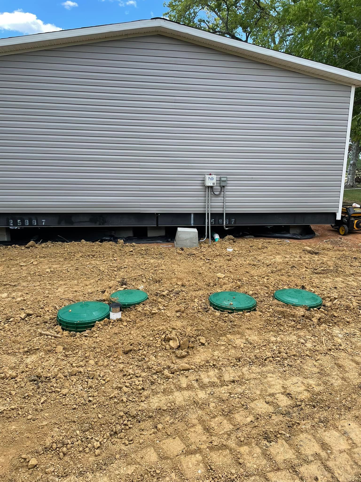 Gray house siding with a gravel yard and four green utility covers near the foundation