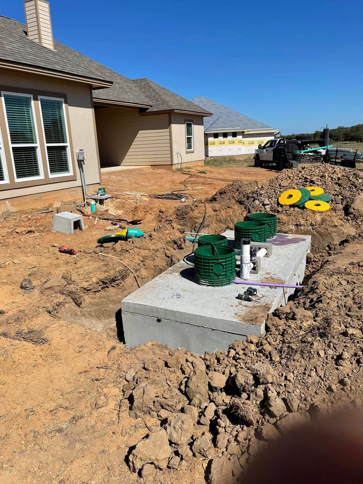 New home construction site with utility boxes, dirt yard, and a house exterior under a clear blue sky