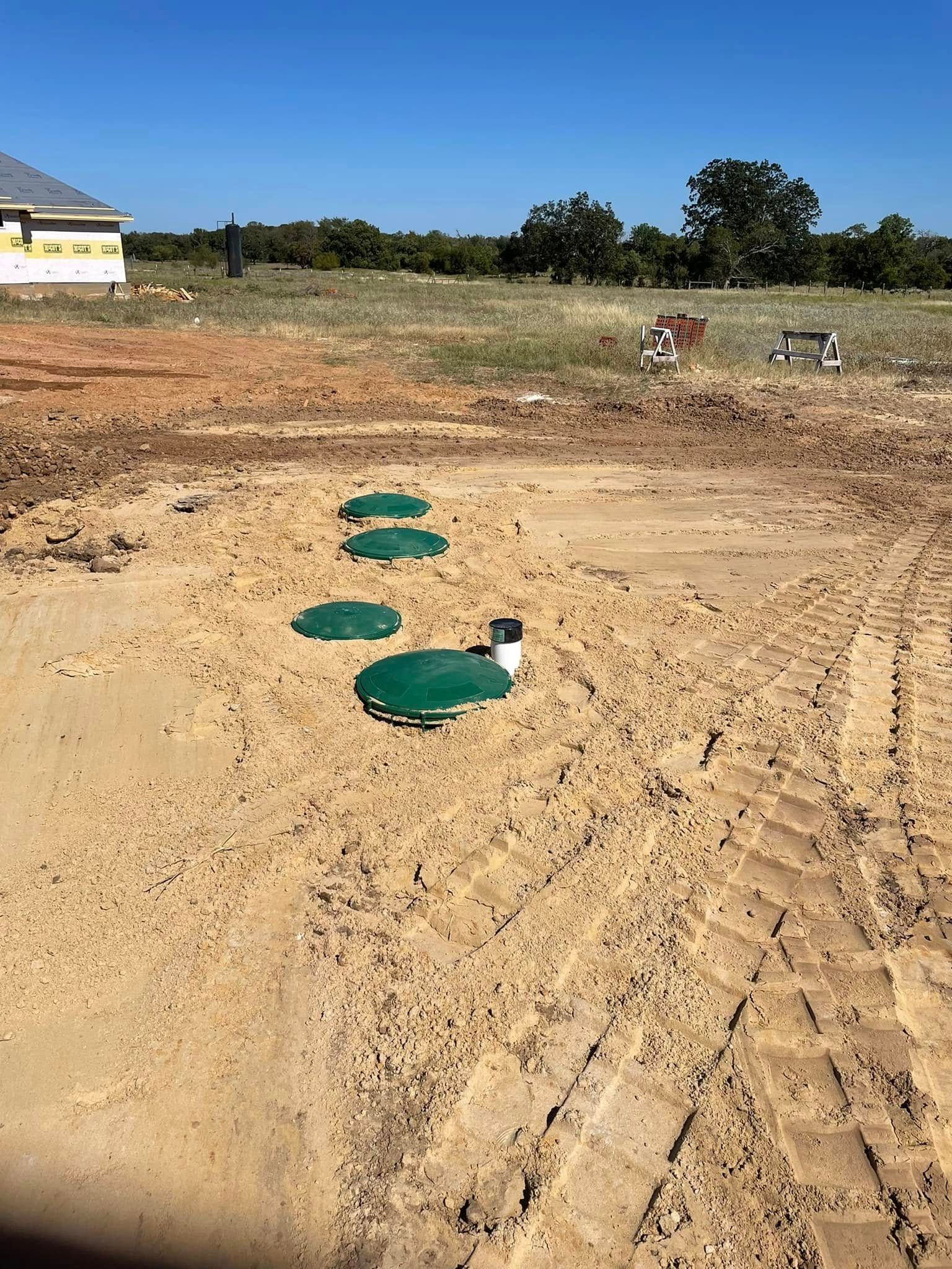 Empty dirt lot with three green utility covers and a small white pipe under a clear sky