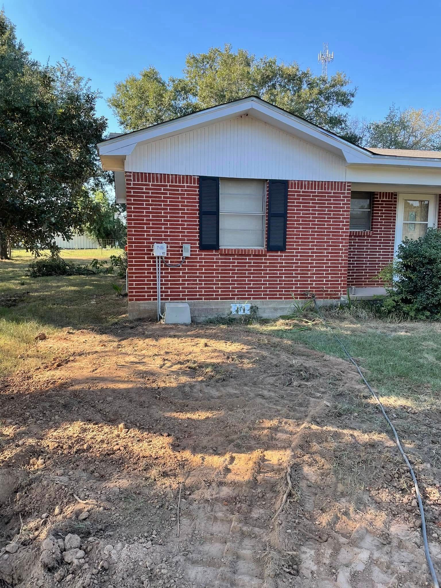 Small brick house with white trim and barred windows, viewed from a dirt yard with trees behind it.