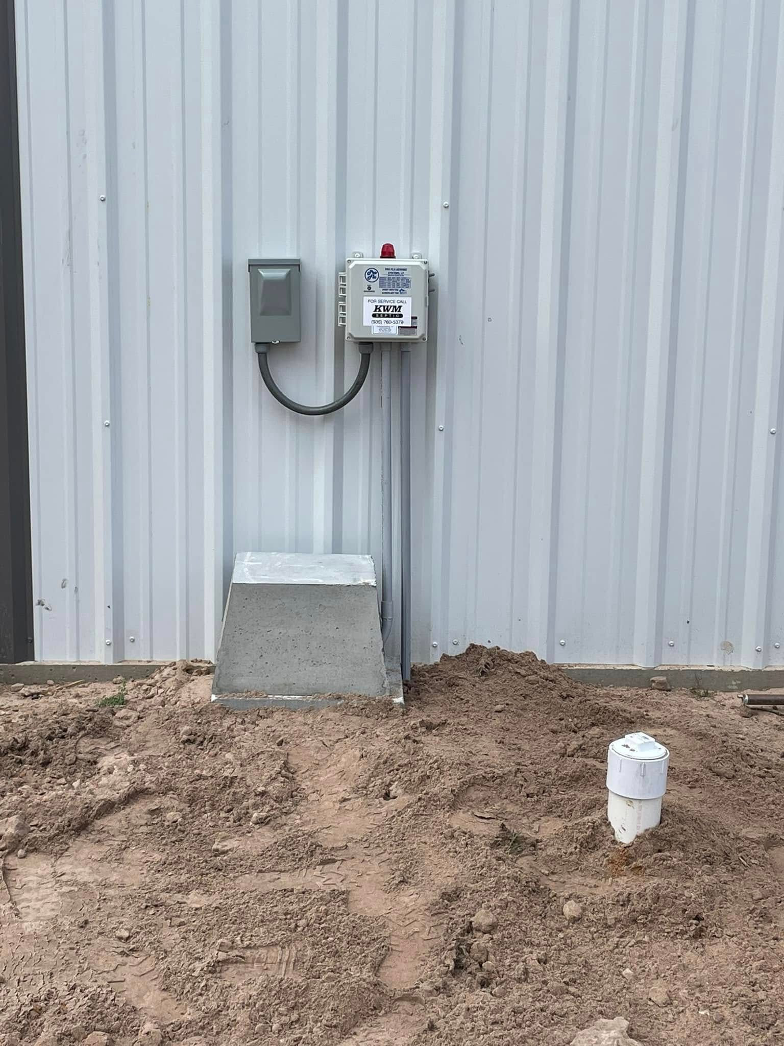 Utility meters on a corrugated metal wall, with a concrete block and dirt foreground.