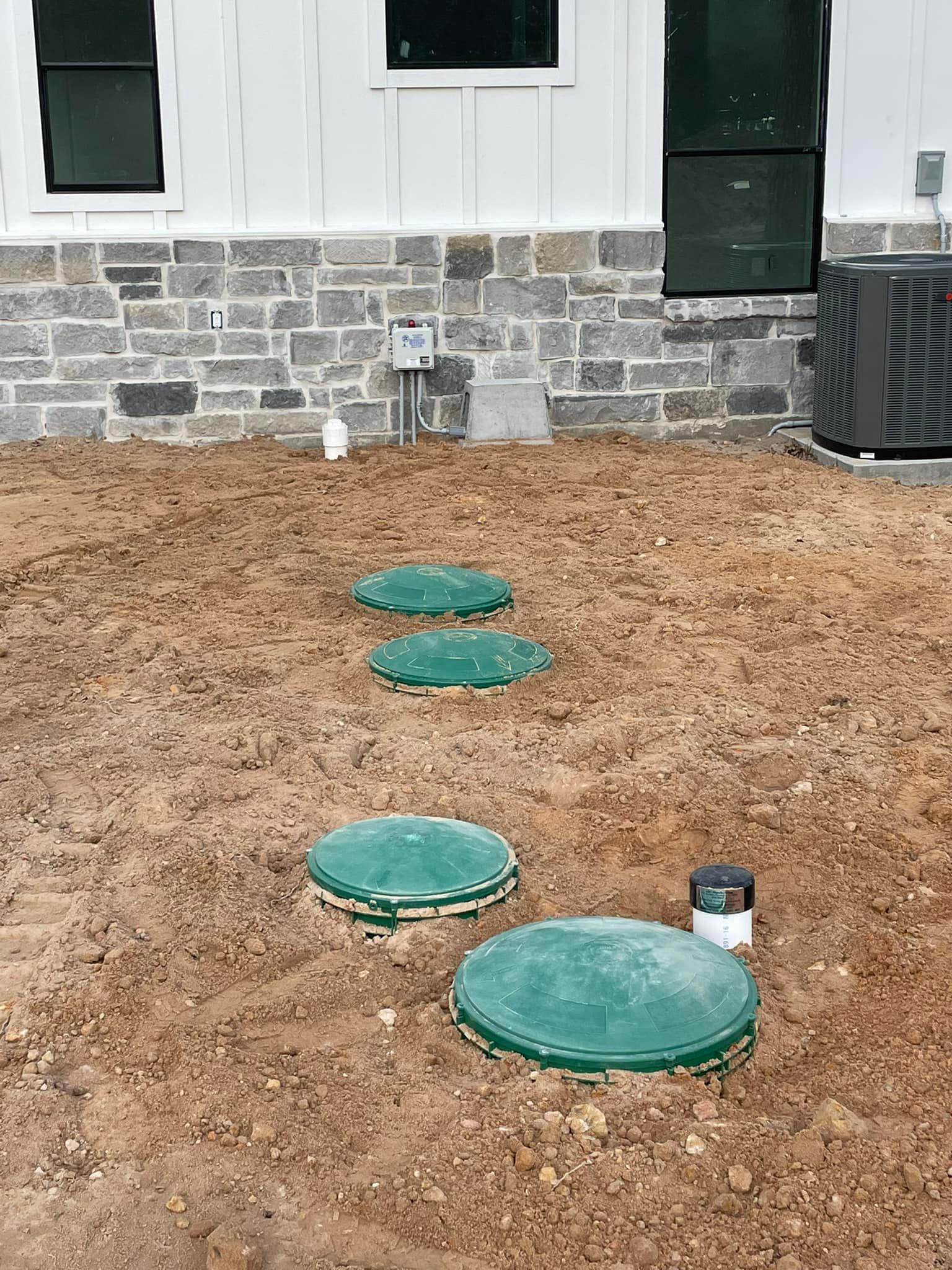 Stone house exterior with mulch-covered yard and four green utility covers leading to the wall.