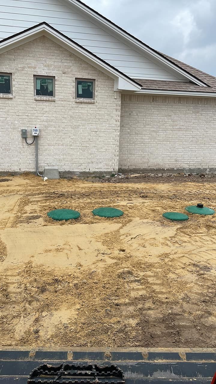 House exterior with unfinished dirt yard and green utility covers near the foundation