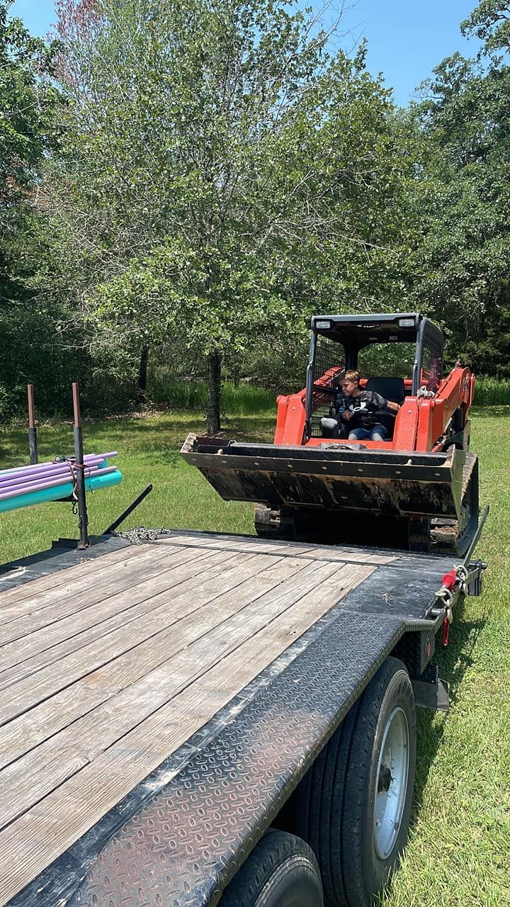 Orange skid steer on a flatbed trailer in a wooded outdoor area