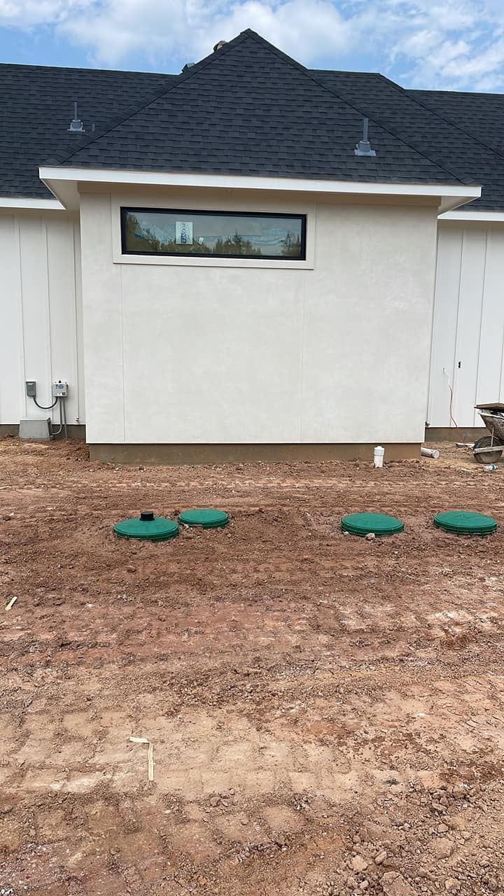 White house exterior with small horizontal window, dirt yard, and several green utility covers in front.