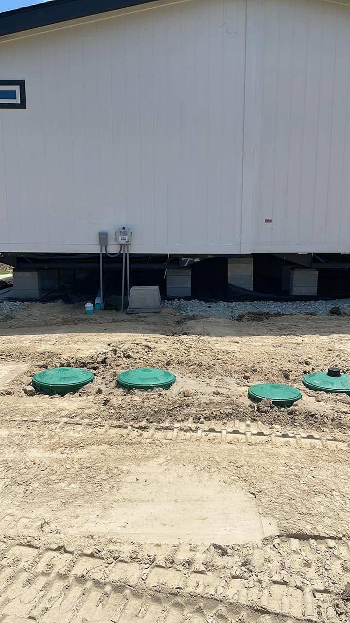 Side of a raised beige building with gravel ground and green utility covers in front