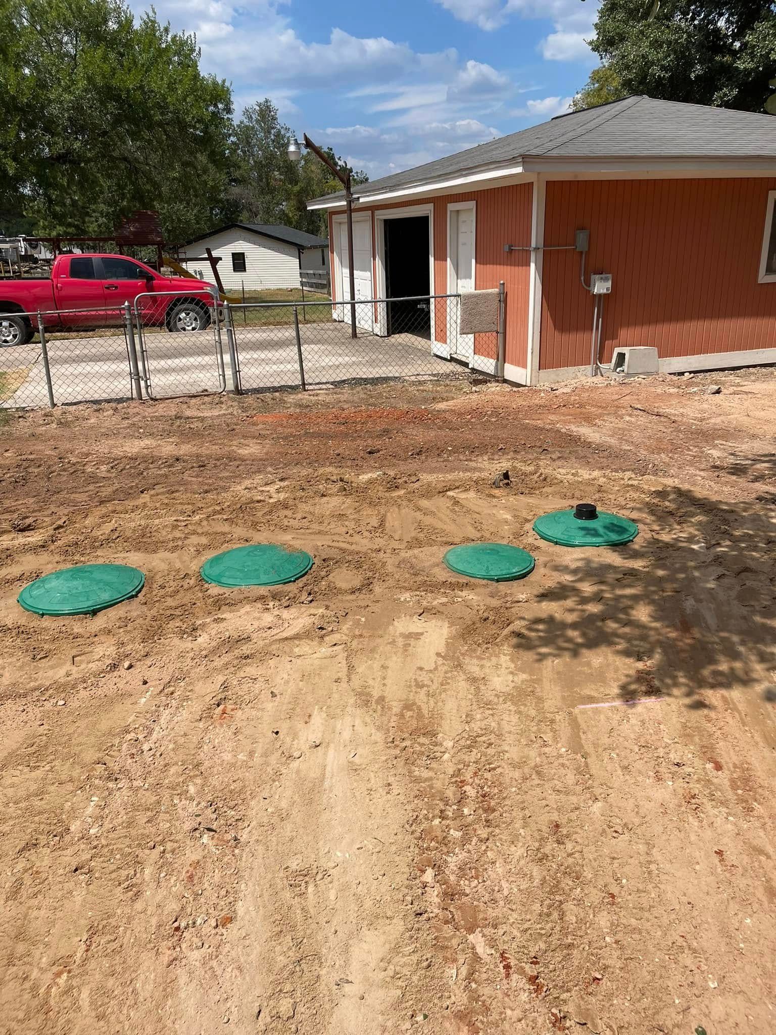 Dirt yard beside a brick house with green utility covers and a red truck in the background